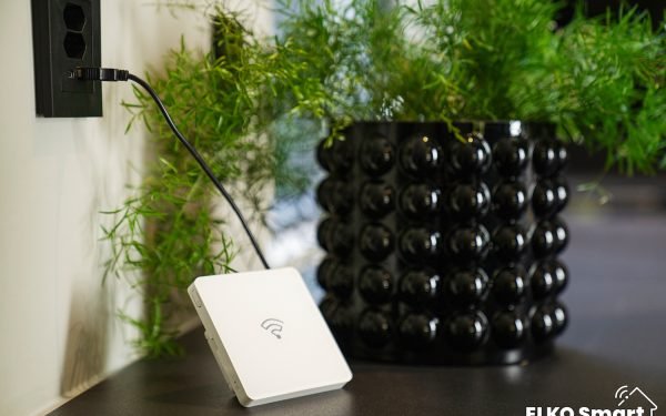 Hvit smarthusenhet med wifi-symbol plassert på et bord ved siden av sort blomsterpotte